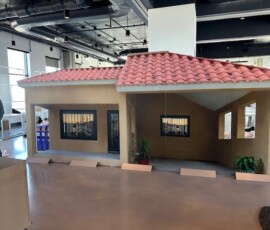Event display featuring life-size house model with red tile roof in exhibition hall